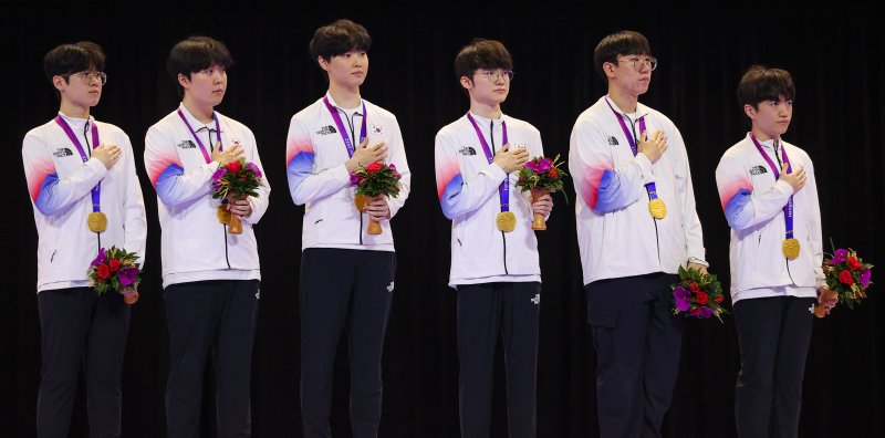 항저우 아시안 게임 리그오브레전드 종목에서 금메달을 수상한 한국 e스포츠 선수단이 시상대에 올라 국기에 경례하고 있다. 왼쪽부터 '제우스' 최우제, '카나비' 서진혁, '쵸비' 정지훈, '페이커' 이상혁, '룰러' 박재혁, '케리아' 류민석. ⓒ사진 연합뉴스